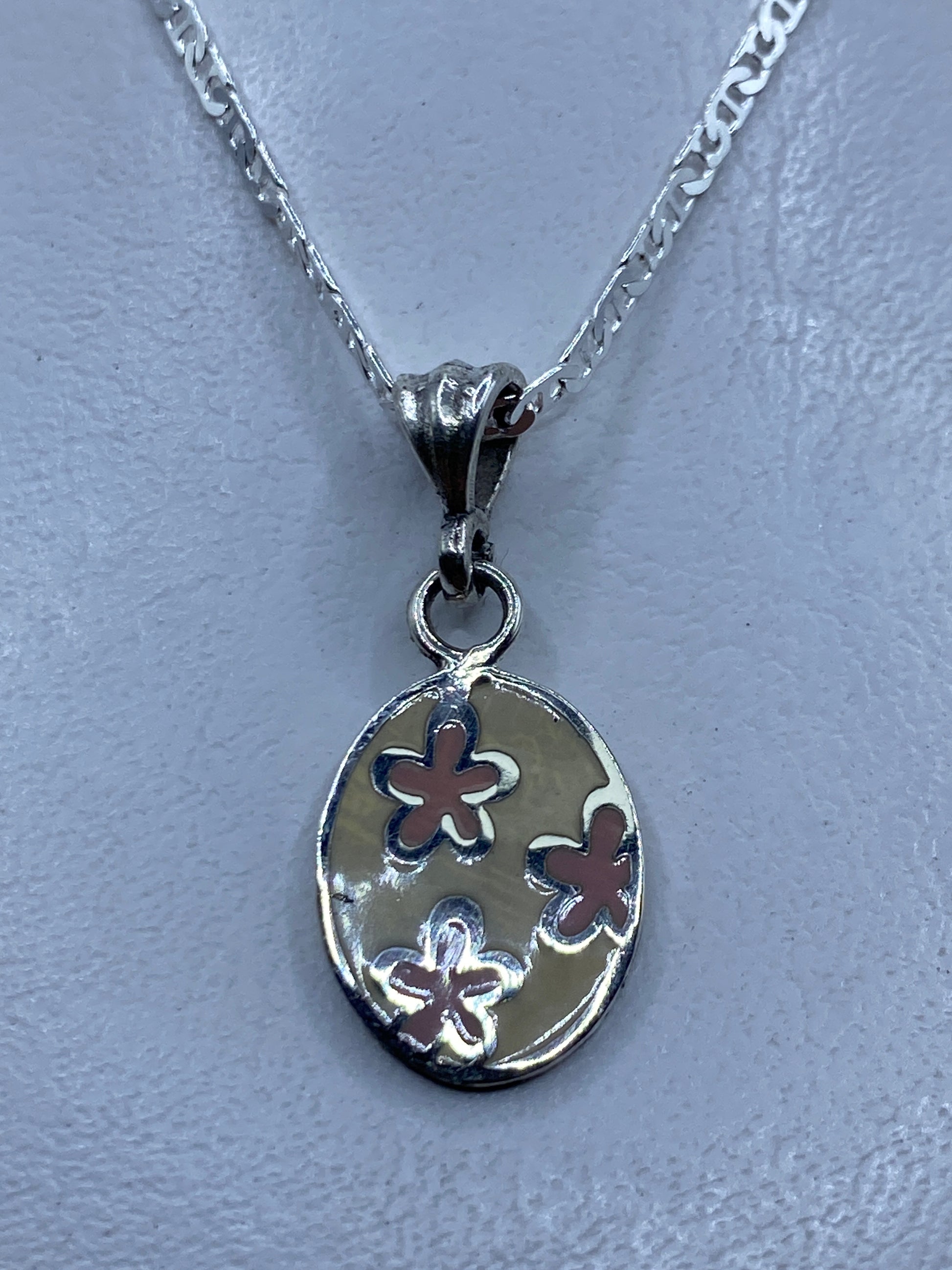Dije de plata con flores en relieve, colgante en cadena plateada sobre fondo gris