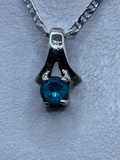 Dije de plata .925 con circonia azul cielo engastada, visto de frente sobre fondo gris