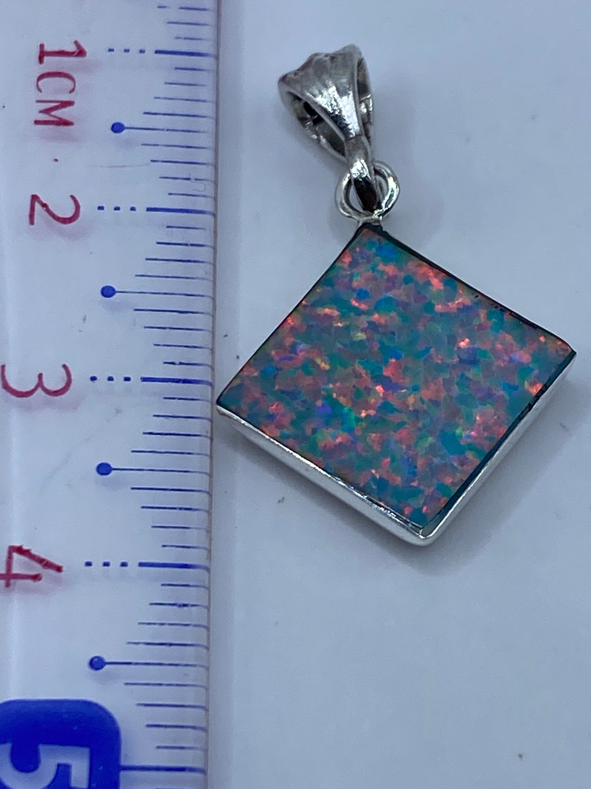 Dije de plata con Ópalo de Fuego sobre regla de centímetros, midiendo 3.3 cm de largo