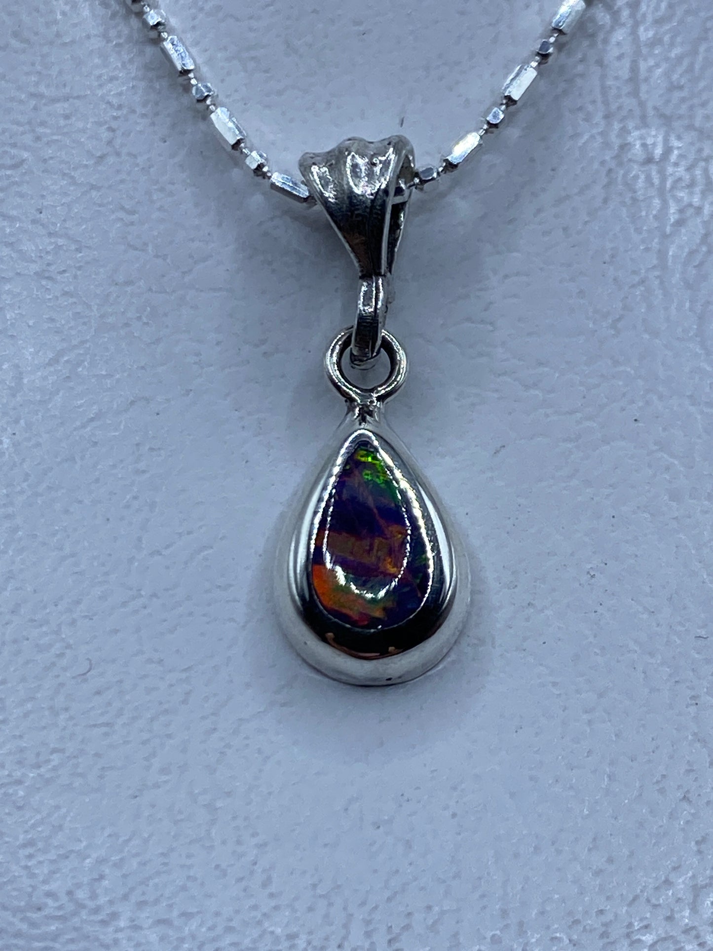 Dije de plata con Opalo de Fuego que refleja tonos naranja y rojo, colgando de una cadena plateada