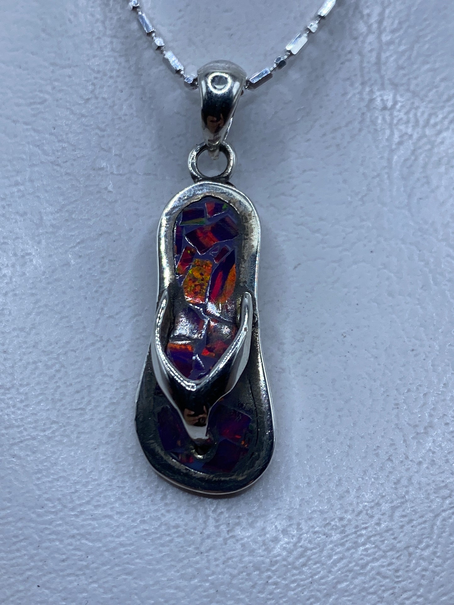 Dije de plata con ópalo de fuego morado engastado, colgando sobre fondo gris