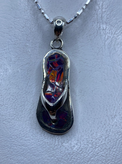 Dije de plata con ópalo de fuego morado engastado, colgando sobre fondo gris