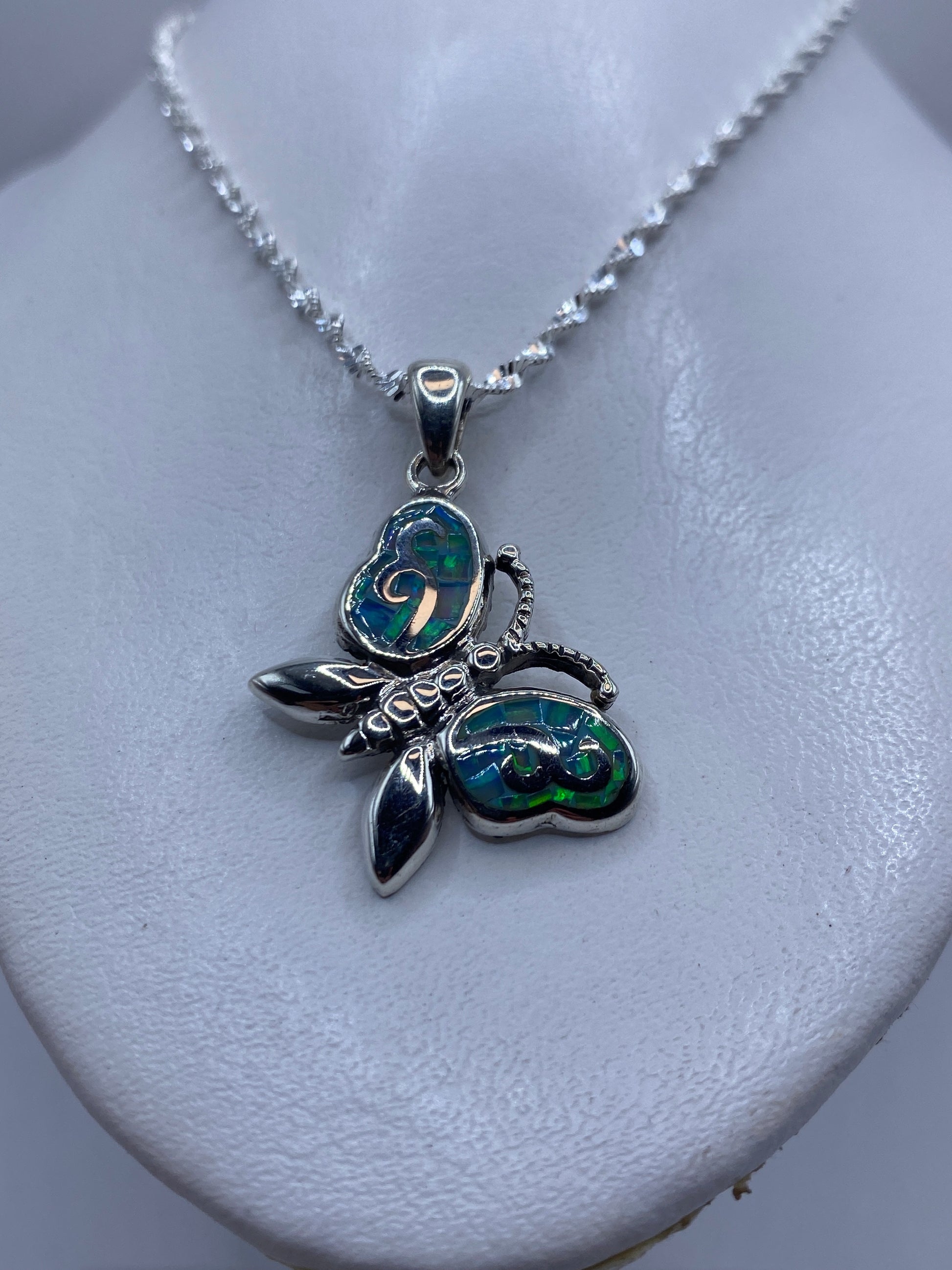 Detalle frontal del dije mariposa mostrando el engaste de ópalo azul y el granulado de las alas