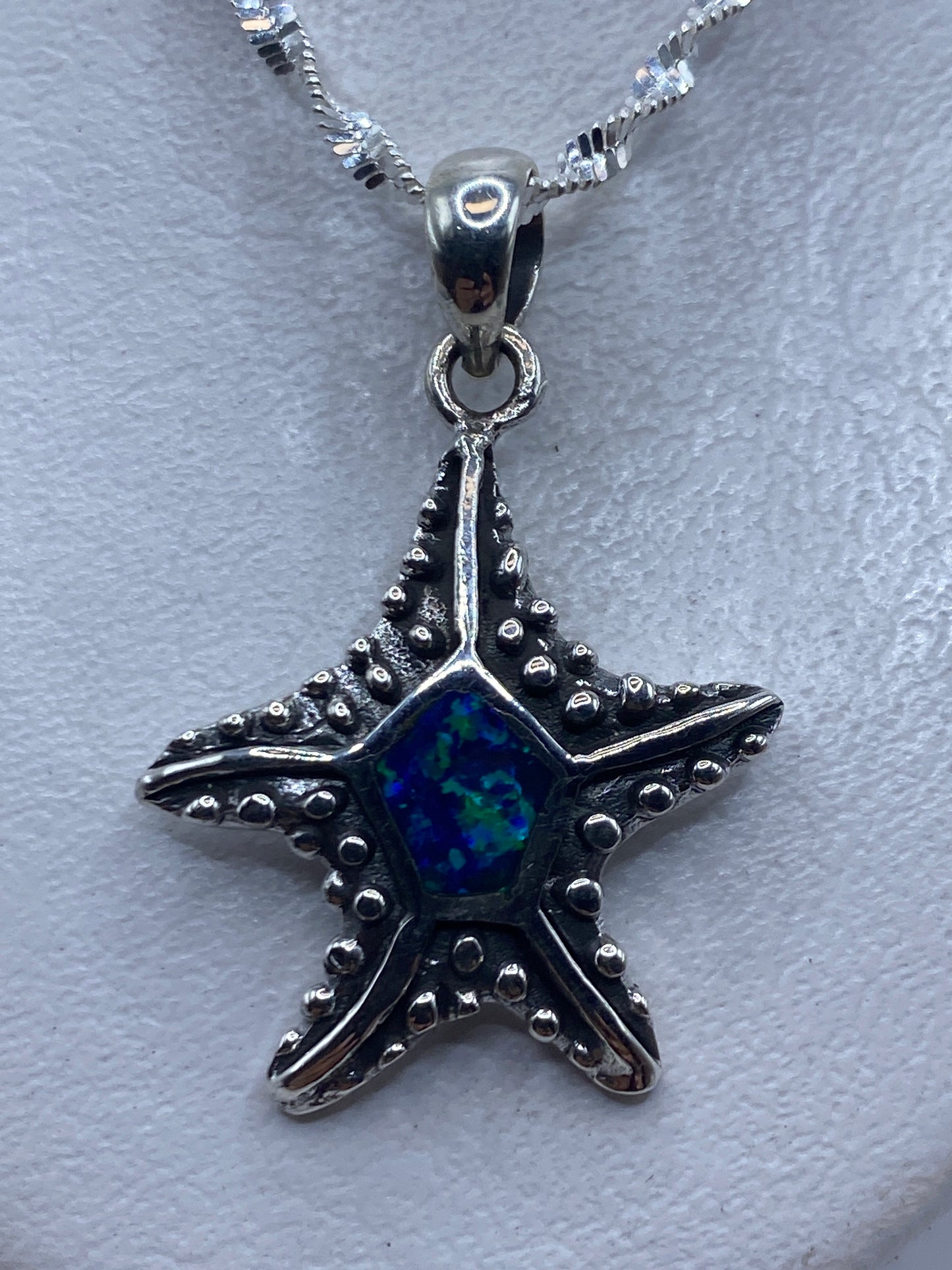 Dije de estrella marina en plata .950 con ópalo de fuego azul, colgante sobre fondo gris