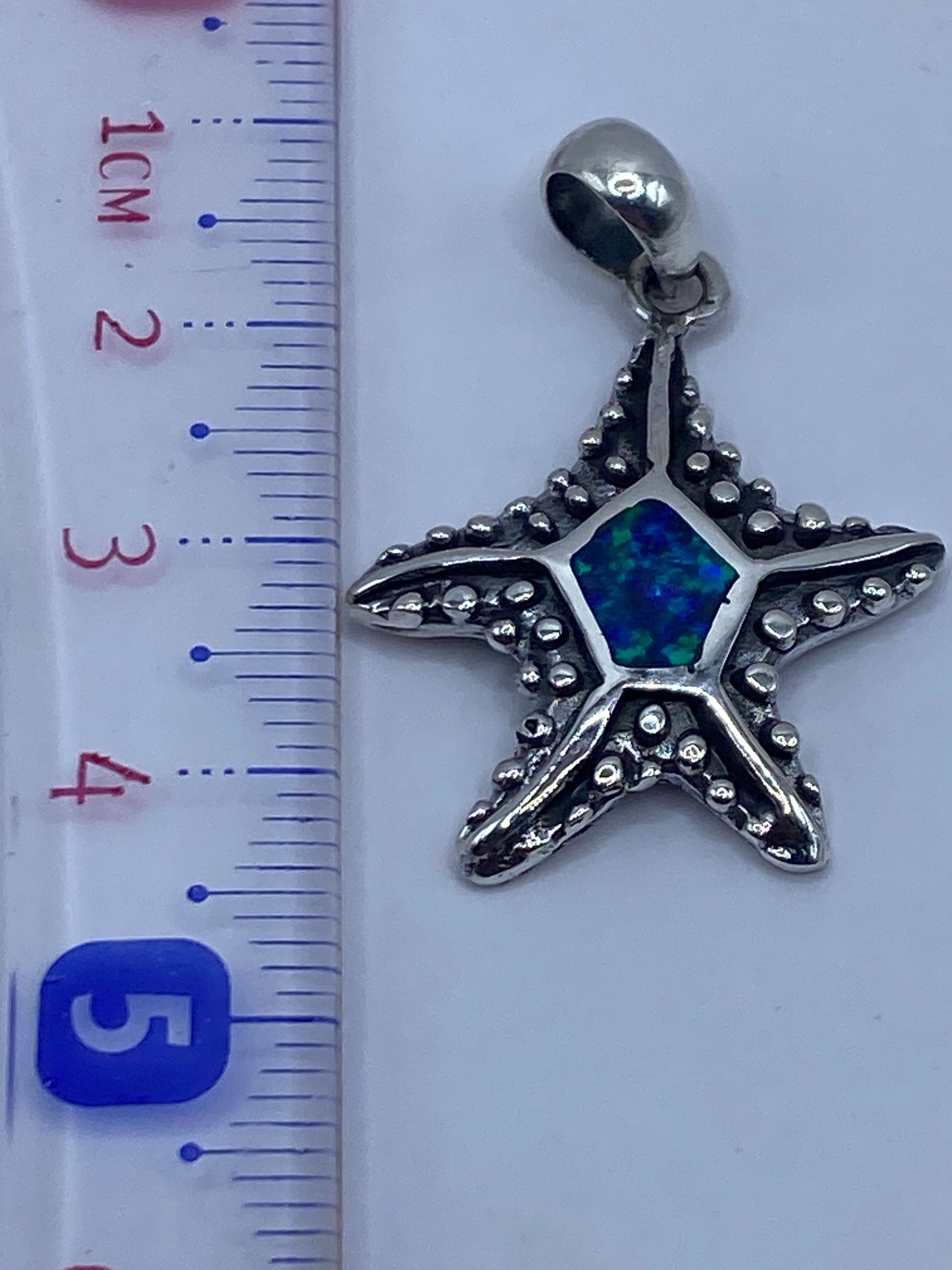 Dije de estrella marina junto a regla métrica mostrando tamaño de 4.5 cm