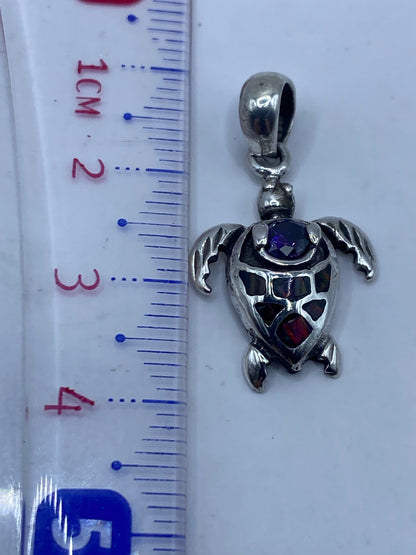 Dije tortuga de 3.6 cm de largo sostenido en la mano para referencia de escala
