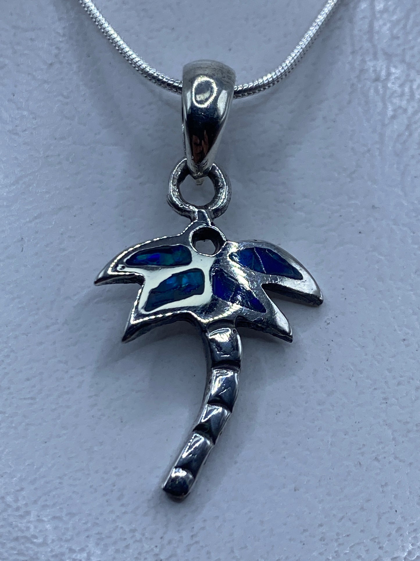 Dije de plata .950 con ópalo de fuego azul engastado a mano, colgando de cadena de plata en el cuello