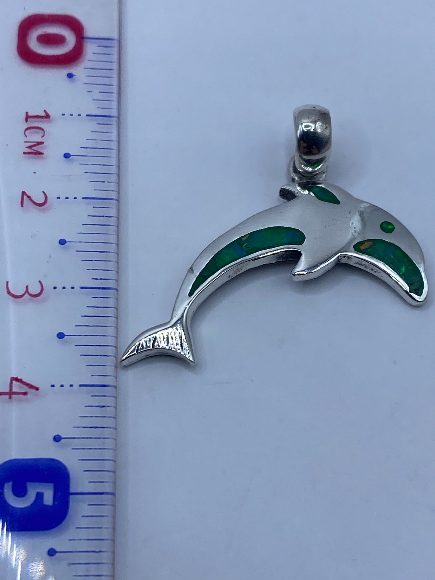 El dije de 4.1 cm junto a una regla de centímetros, mostrando su tamaño real