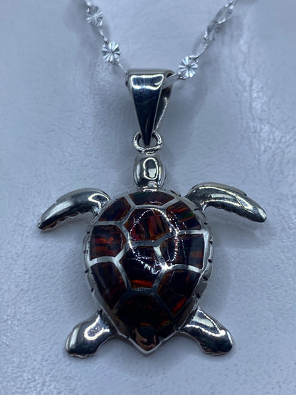 Dije tortuga en plata .950 con ópalo de fuego multicolor rojo y naranja, colgando de cadena de plata delgada