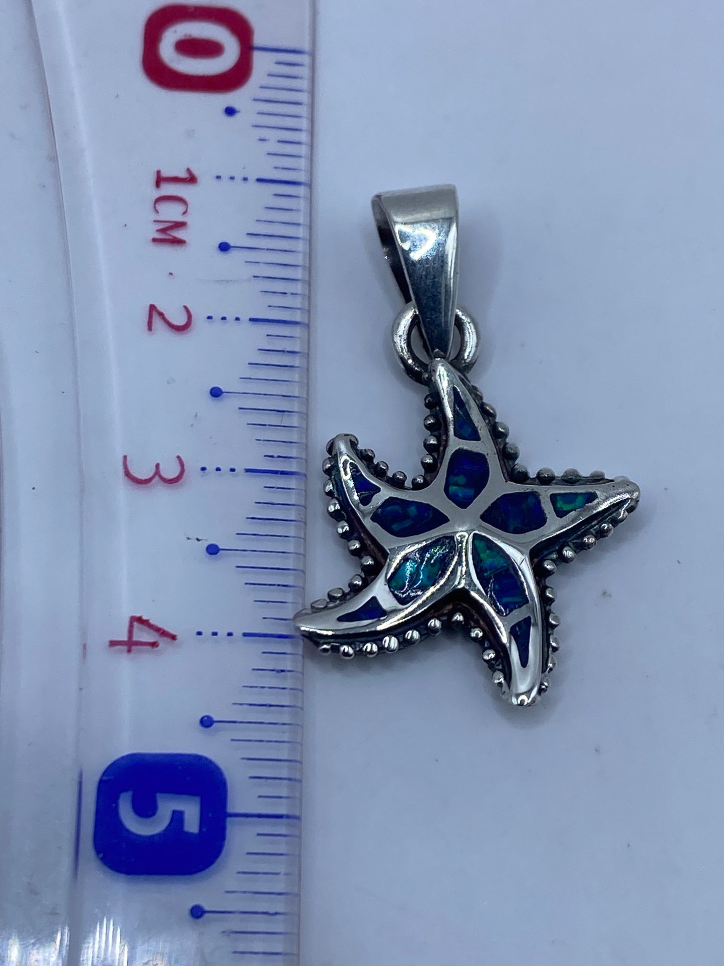 Dije en escala junto a regla: 4.3 cm de largo, con sello .950 visible en la plata