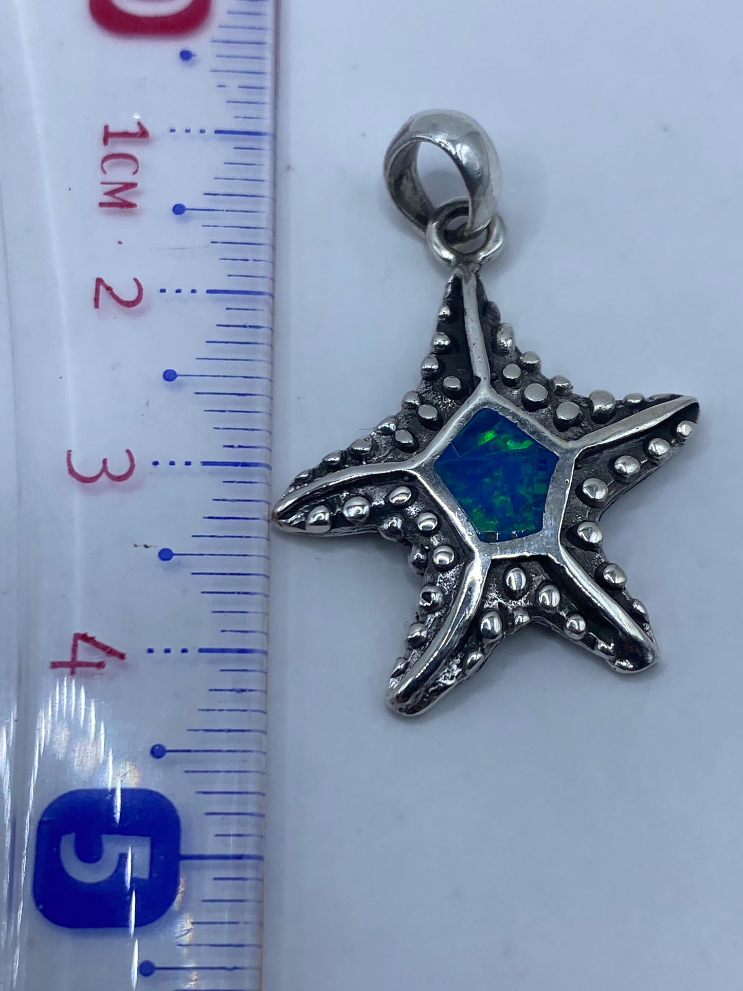 Dije estrella de mar en balanza de precisión junto a regla, 4.2 cm de largo, 3.8 gramos