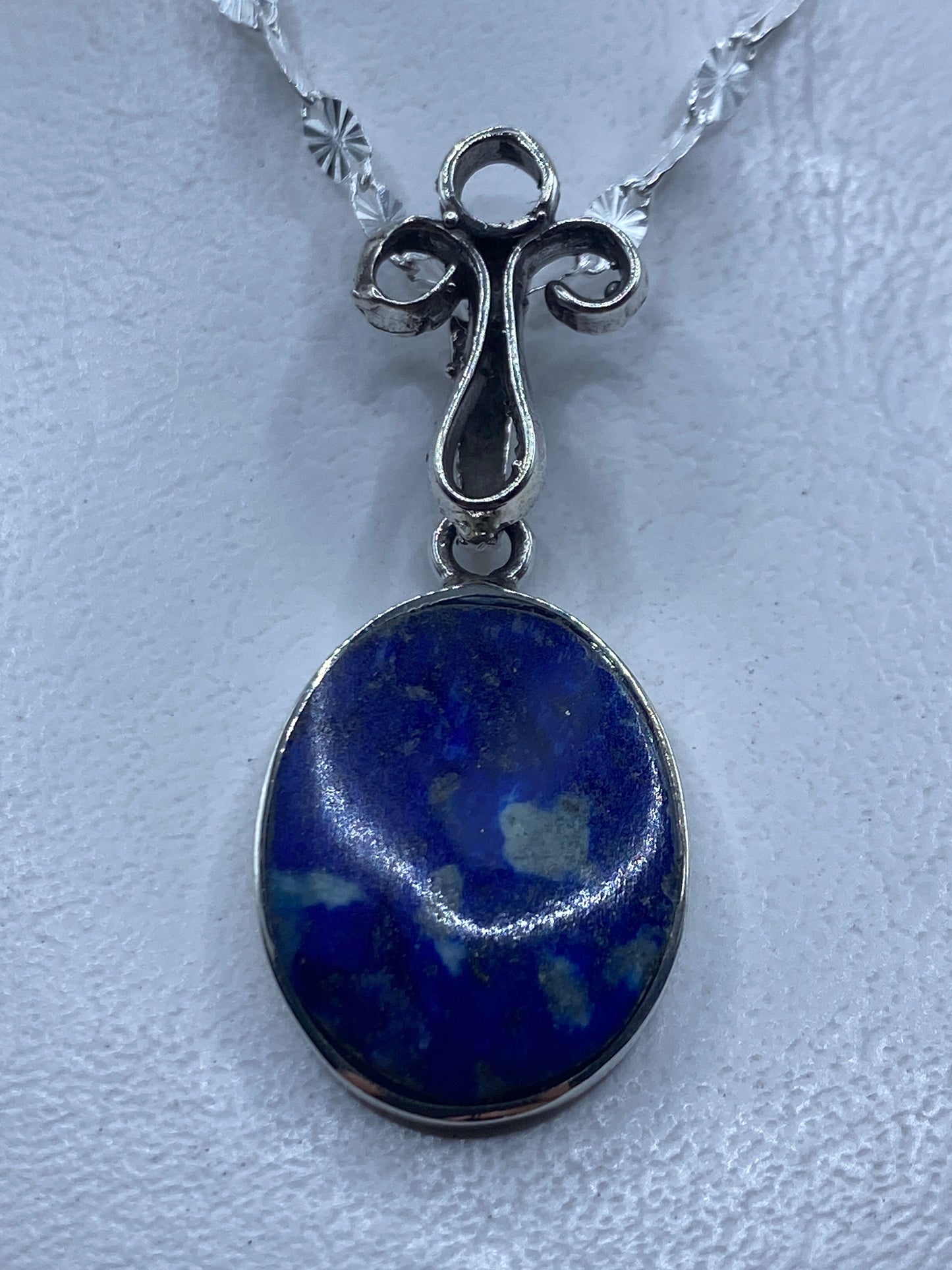 Dije de plata .925 con piedra azul engastada, colgando de una cadena de plata