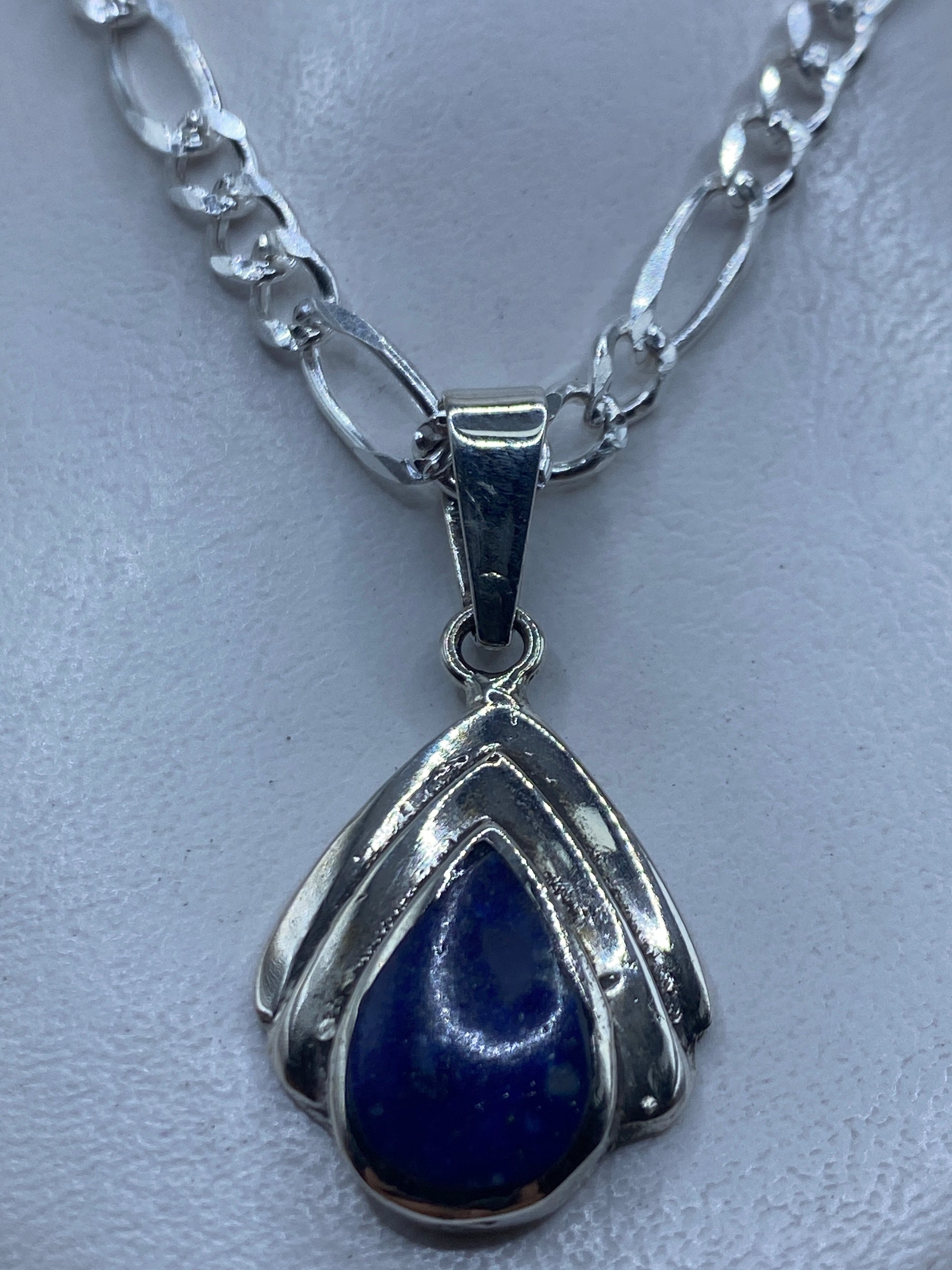 Dije de plata en forma de gota con piedra azul engastada, colgando de cadena plateada en el cuello