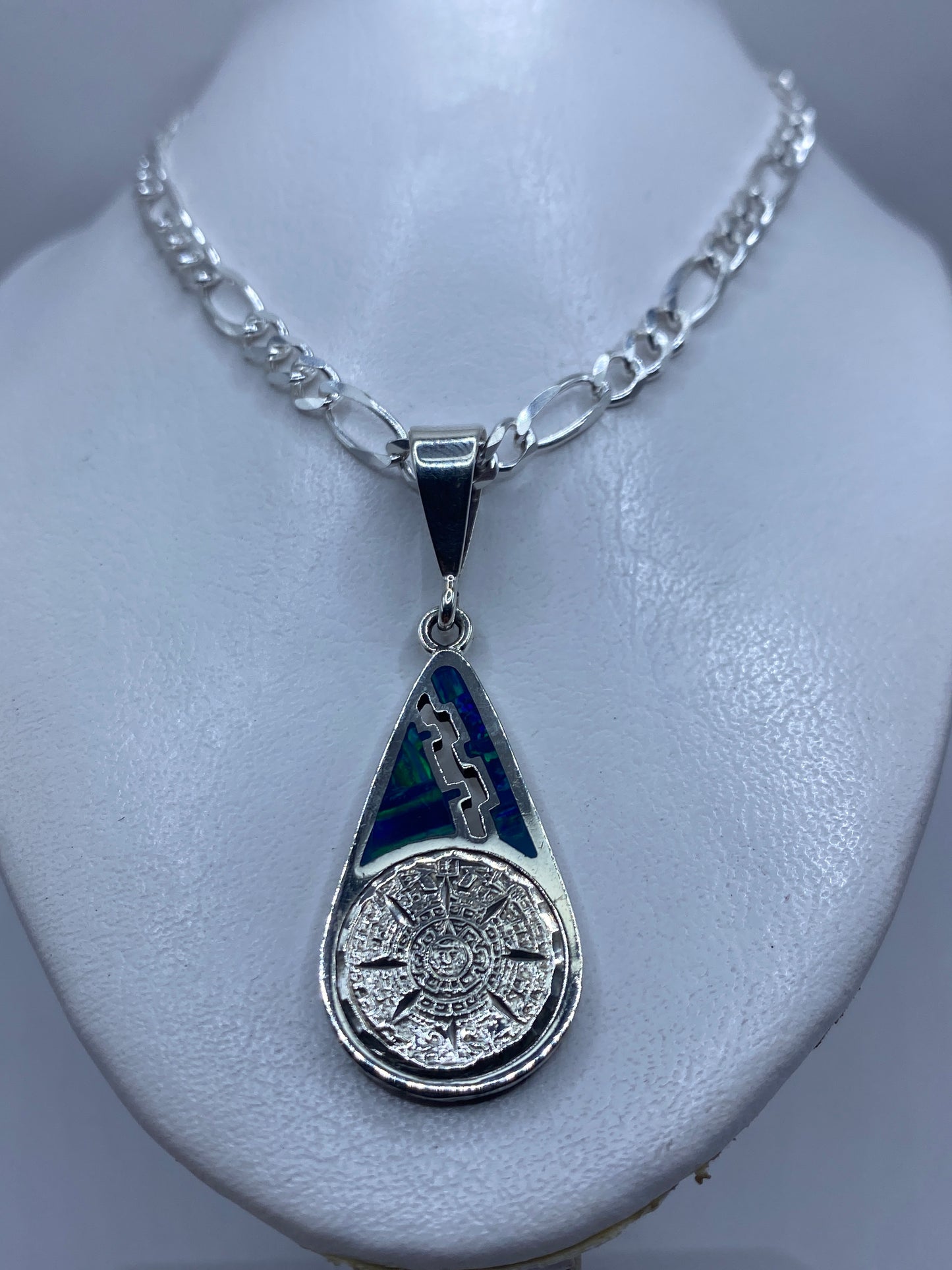 Detalle frontal del dije: calendario prehispánico tallado en plata con ópalo azul verdoso