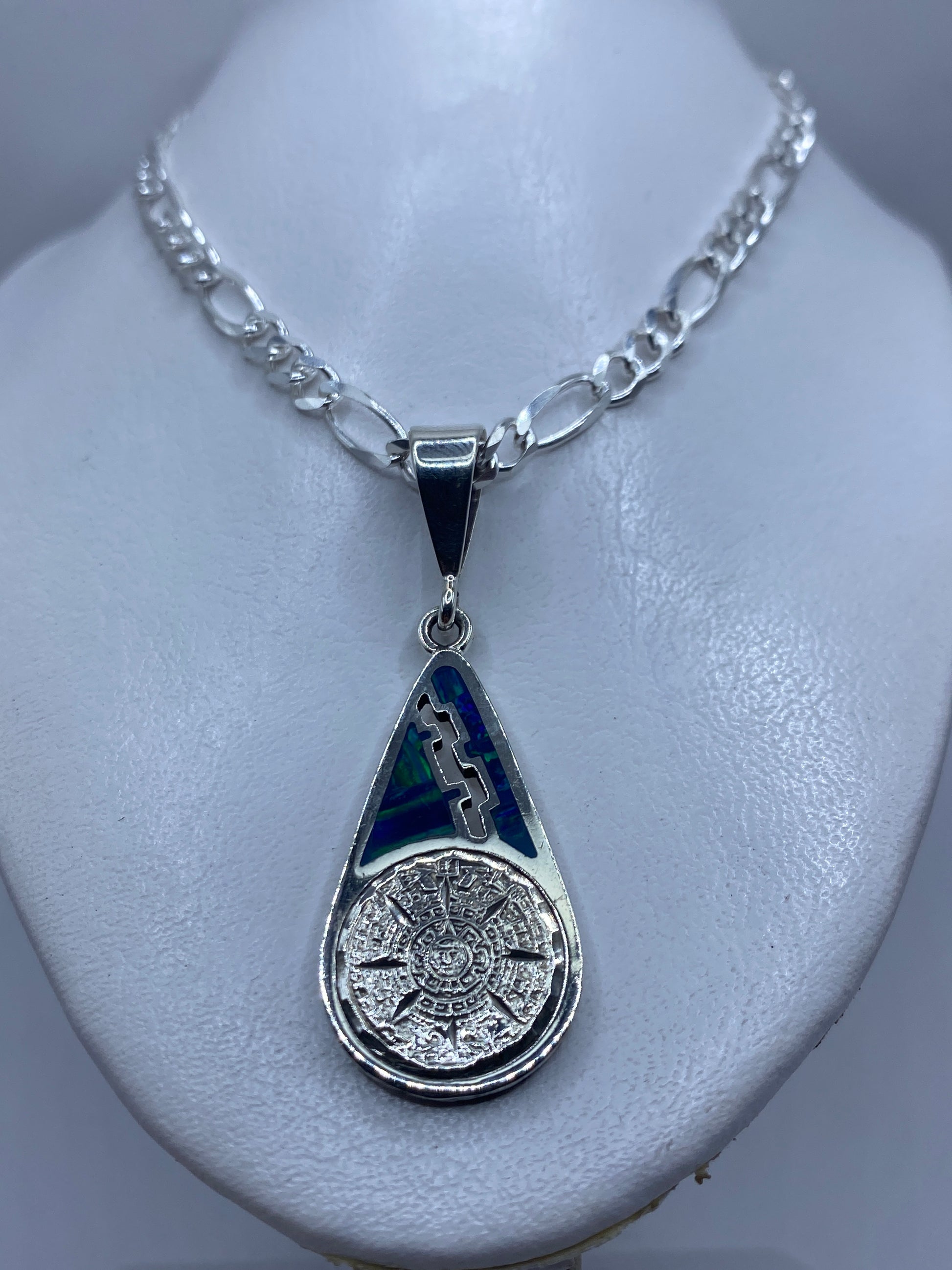 Detalle frontal del dije: calendario prehispánico tallado en plata con ópalo azul verdoso
