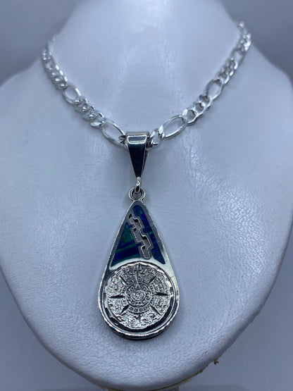 Detalle frontal del dije: calendario prehispánico tallado en plata con ópalo azul verdoso