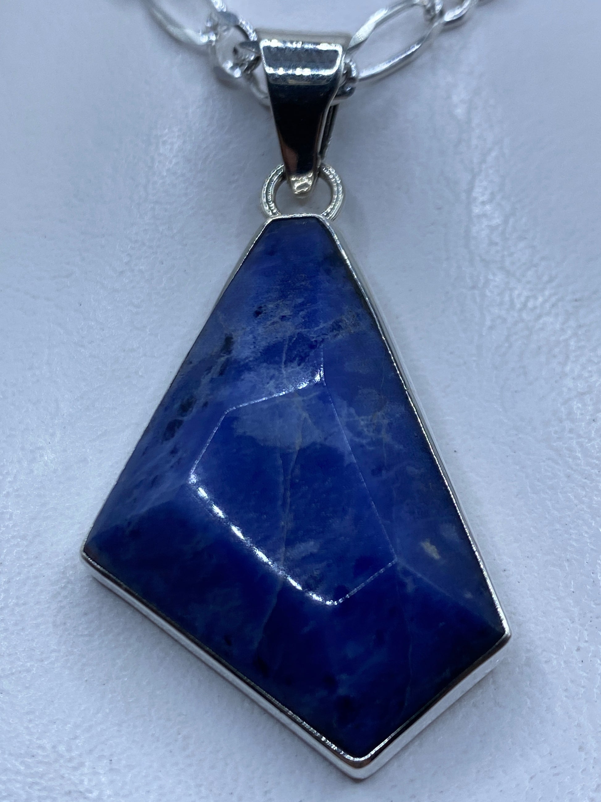 Dije de plata .950 con piedra azul engastada, colgando de cadena de plata en cuello