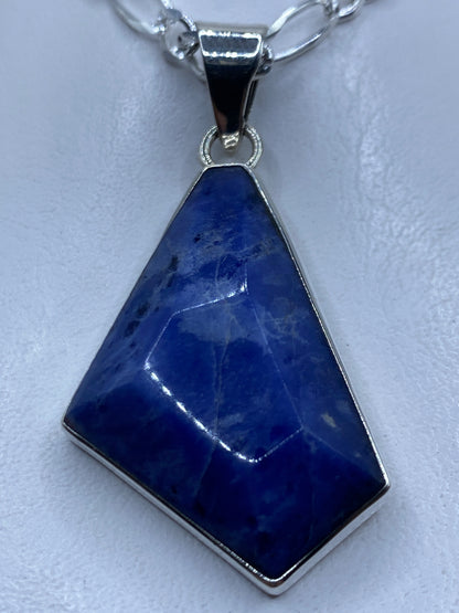 Dije de plata .950 con piedra azul engastada, colgando de cadena de plata en cuello