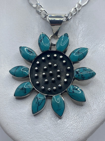 Dije floral de plata .925 con diez pétalos de turquesa azul cielo en mano de mujer