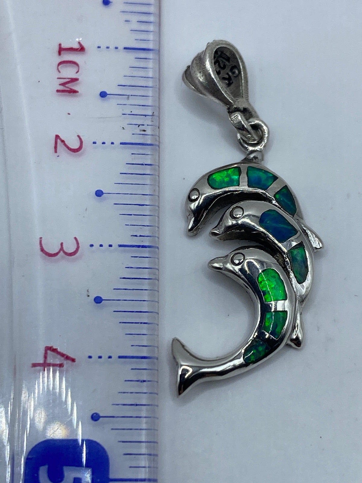 Dije de delfín de 4.3 cm sobre regla métrica, mostrando escala real