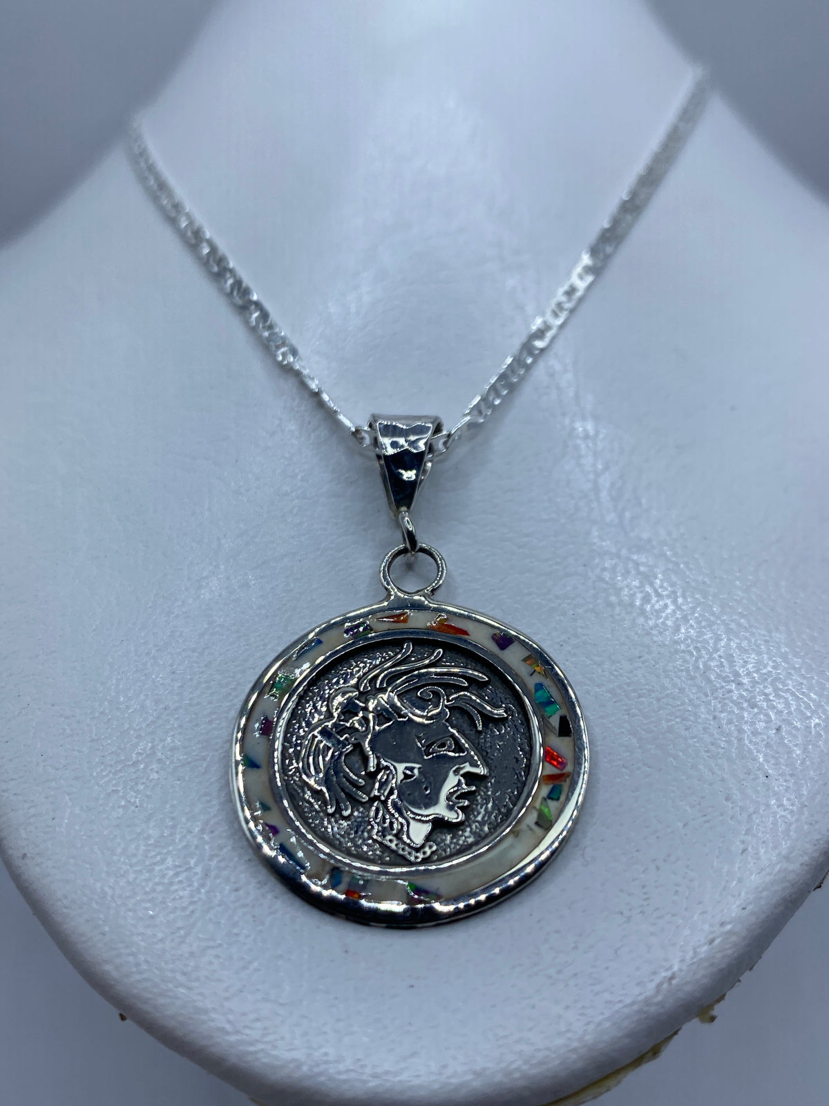 Dije sobre pecho — diseño geométrico prehispánico brilla en plata y luz de ópalo