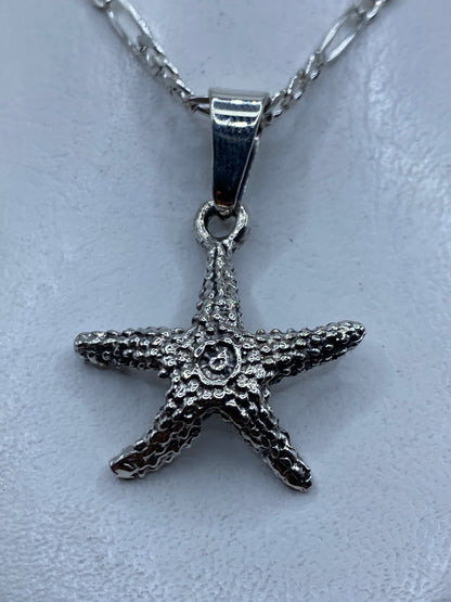Dije de plata granulado con forma de estrella de mar, colgando de cadena, primer plano detalle