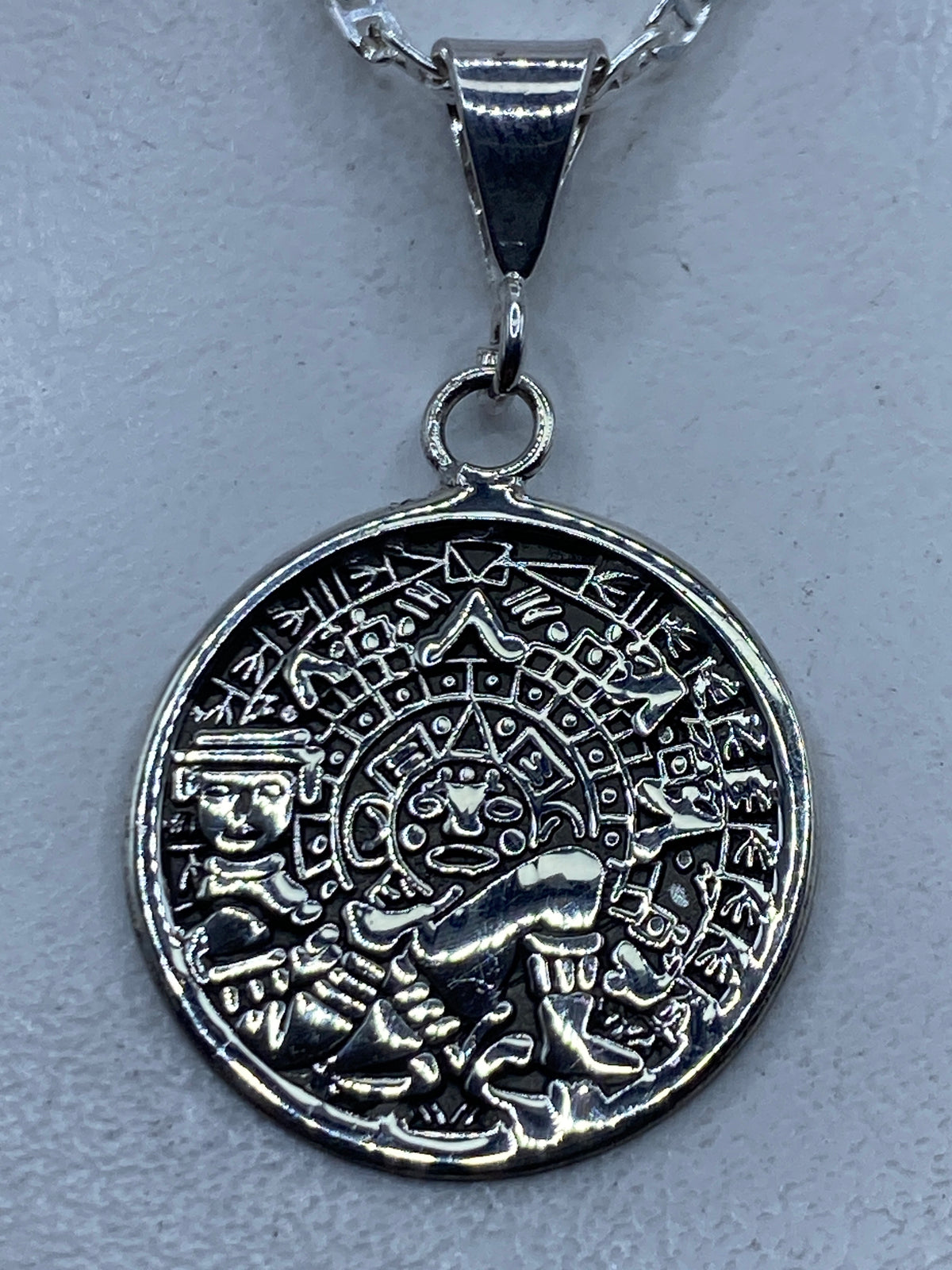 Dije de plata repujado con calendario azteca de frente, sobre cadena de plata