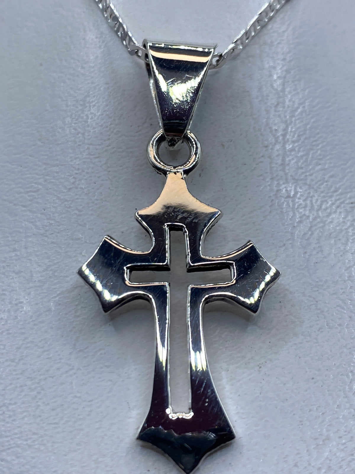 Dije cruz de plata .925 pulida sobre fondo gris, visto desde arriba