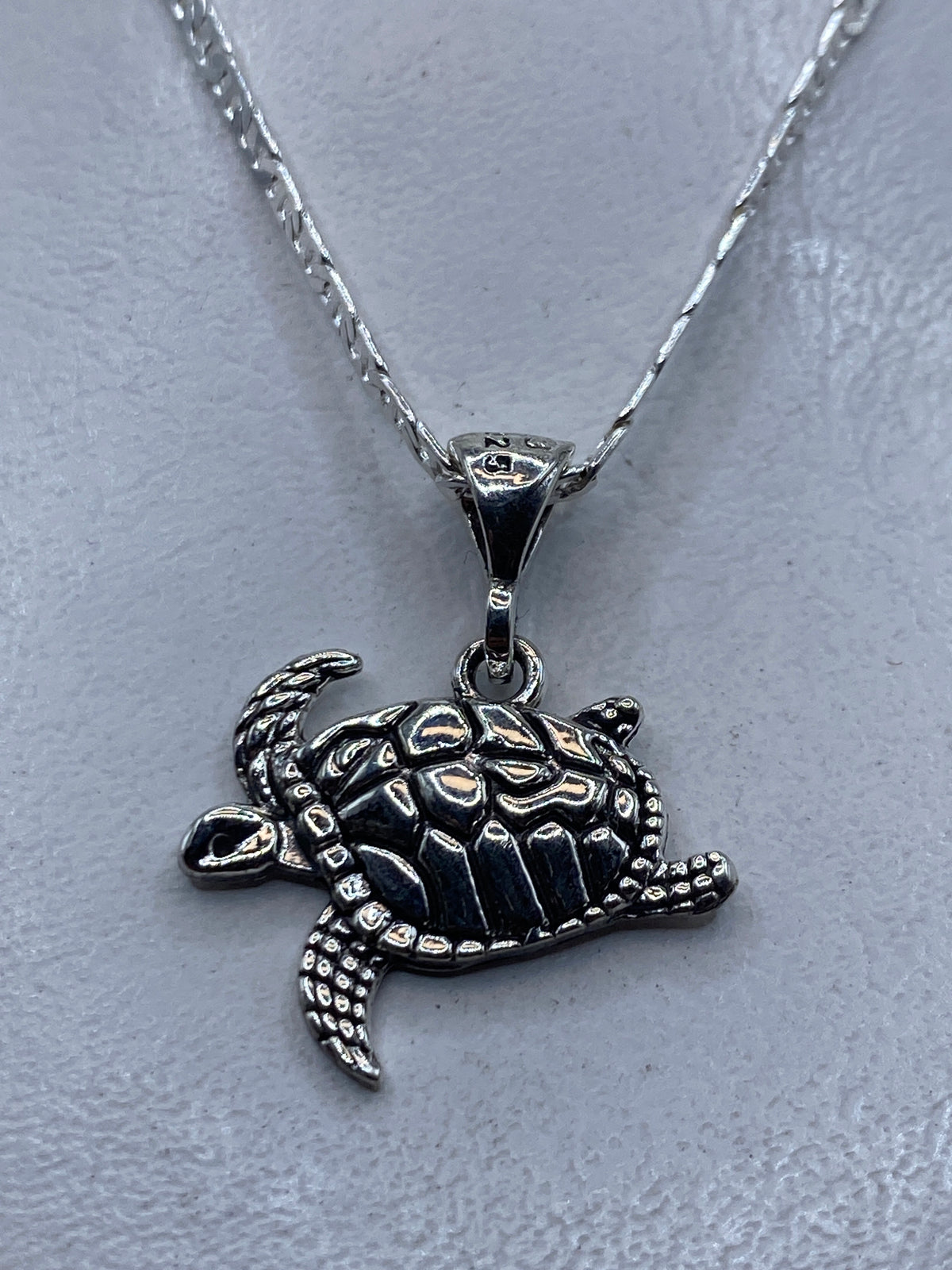 Dije de tortuga marina en plata repujada, colgado de cadena de plata en el cuello