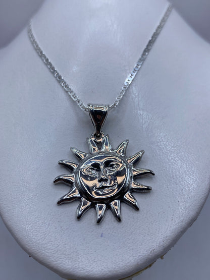 Detalle frontal del dije sol de fundición artesanal con cara antropomórfica y acabado pulido brillante
