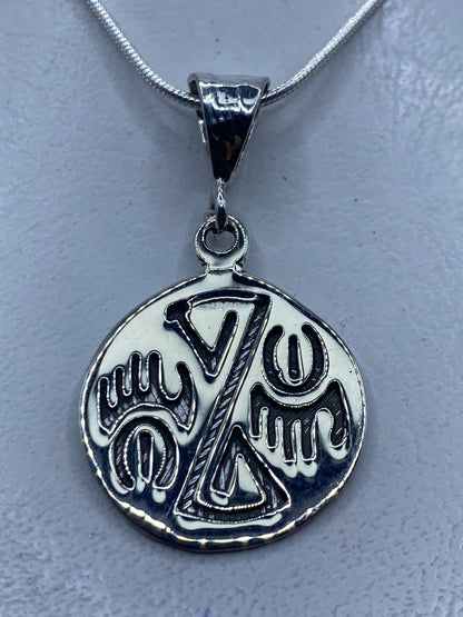 Dije de plata repujado con diseño prehispánico, colgado de cadena de plata en el cuello