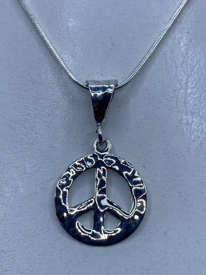 Dije de paz en plata repujada de Taxco .925, 3.7 cm, colgando de cadena plateada