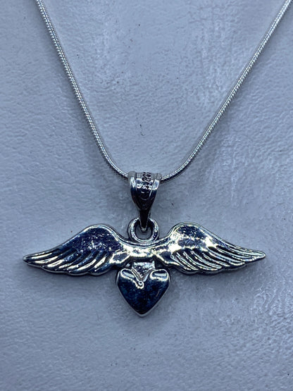 Dije de plata con alas abiertas y corazón central, sobre collar de cadena serpiente