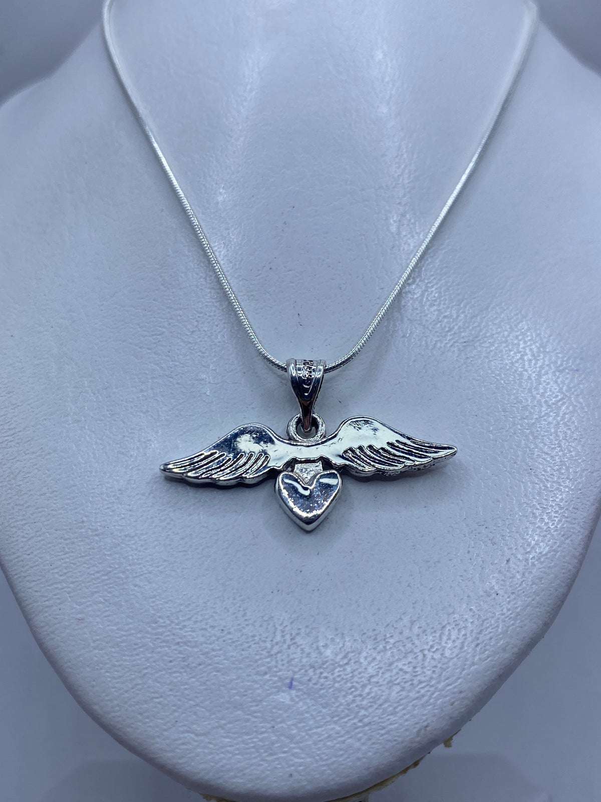 Detalle frontal del dije de alas y corazón mostrando el acabado pulido