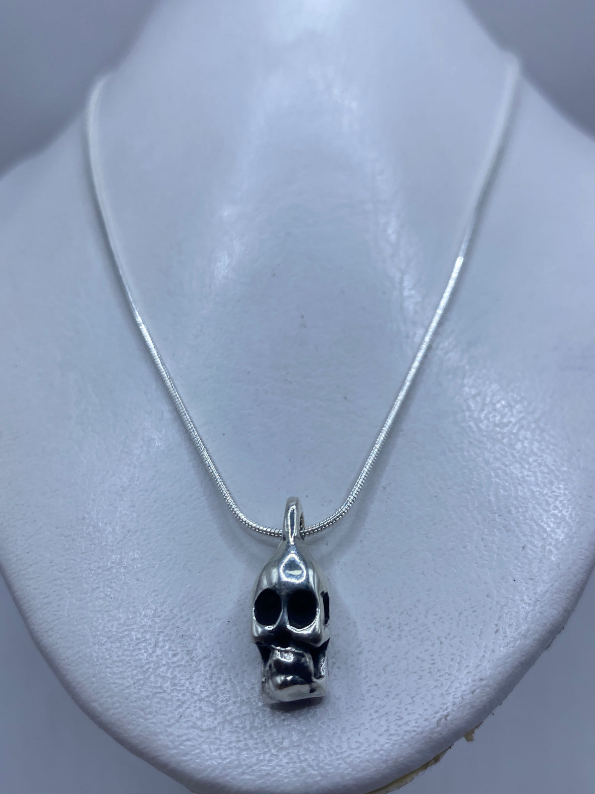 Vista frontal del dije calavera minimalista en plata pulida