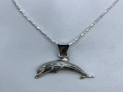 Dije de plata .925 con forma de delfín grabado en relieve, colgando de cadena plateada