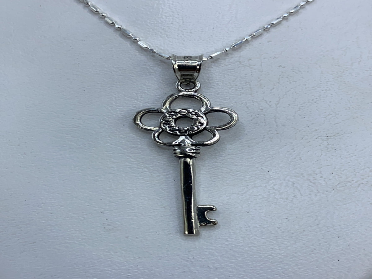 Dije de plata calado en forma de llave floral, largo 4 cm, sobre fondo blanco