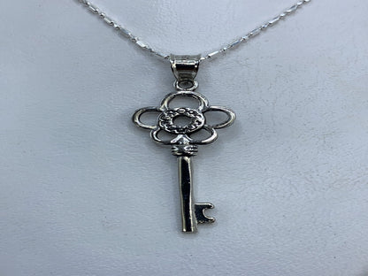 Dije de plata calado en forma de llave floral, largo 4 cm, sobre fondo blanco