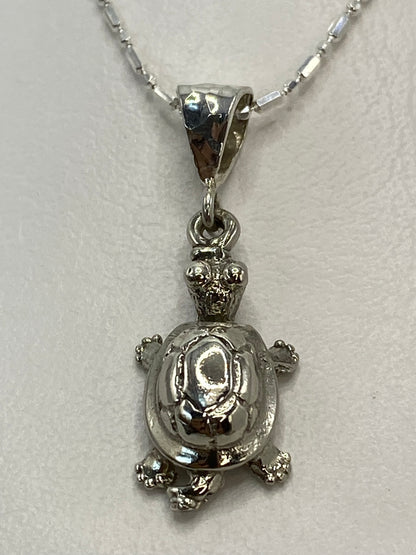 Dije de tortuga en plata repujada colgando de una cadena delgada
