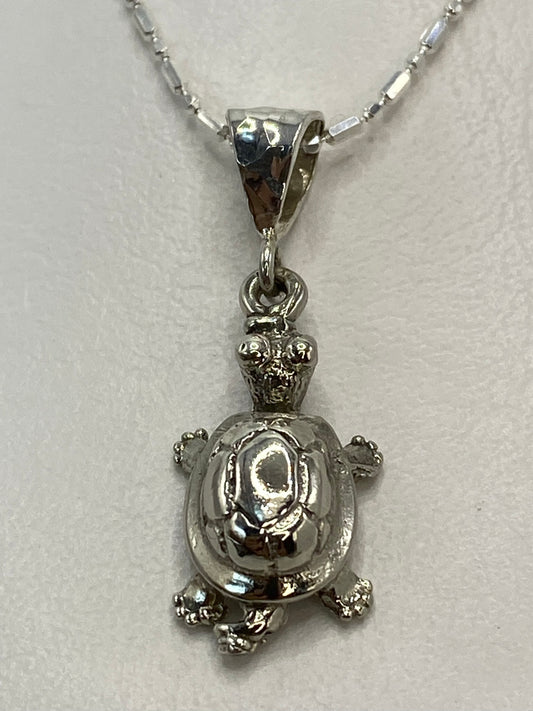 Dije de tortuga en plata repujada colgando de una cadena delgada
