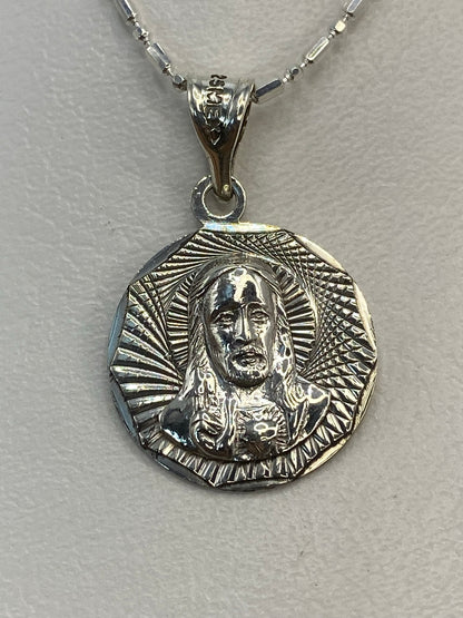 Dije de plata repujado con figura religiosa y nimbo radiante, colgando de cadena plateada