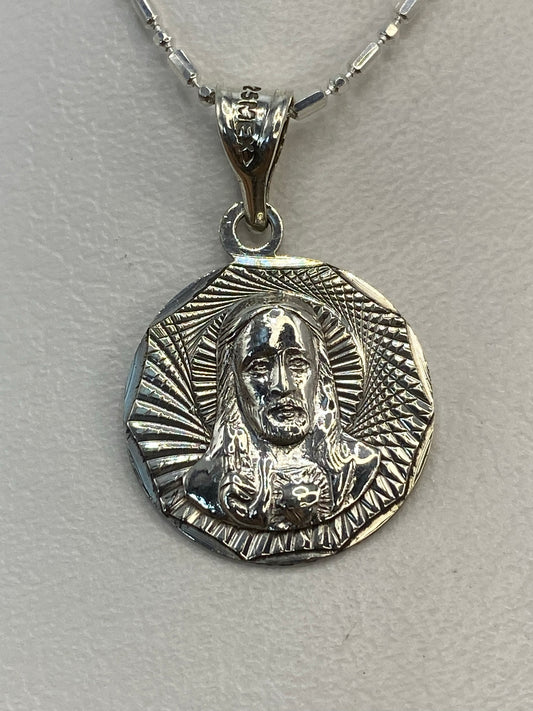 Dije de plata repujado con figura religiosa y nimbo radiante, colgando de cadena plateada