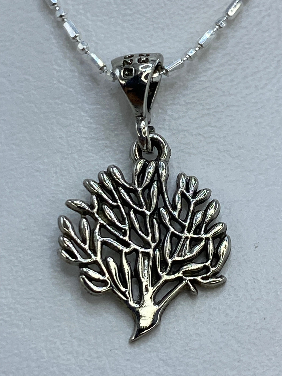 Dije de hoja de plata con corte calado colgando de cadena de bolitas