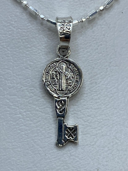 Dije de plata repujado con San Benito y llave en la palma de una mano