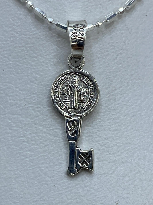 Dije de plata repujado con San Benito y llave en la palma de una mano