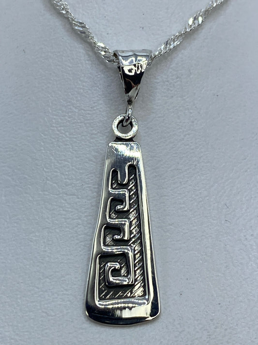 Dije de plata repujado con espiral prehispánica, 3 cm de largo, colgando de una cadena plateada