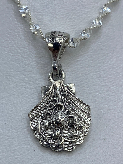Dije de plata en forma de concha con detalles calados, colgante sobre fondo blanco