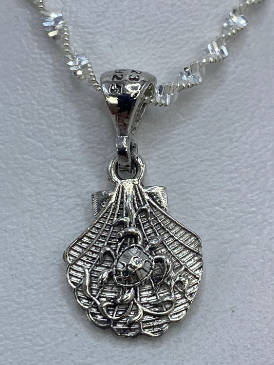 Dije de plata en forma de concha con detalles calados, colgante sobre fondo blanco