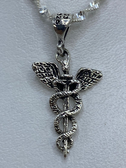 Dije caduceo de 3 cm sobre fondo blanco con sello .925 visible