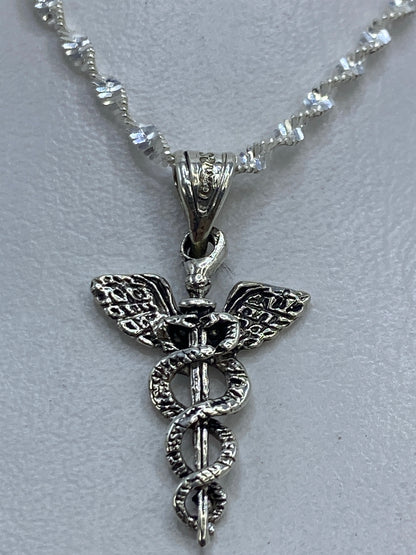 Dije de plata caduceo médico de 2 cm sobre fondo gris